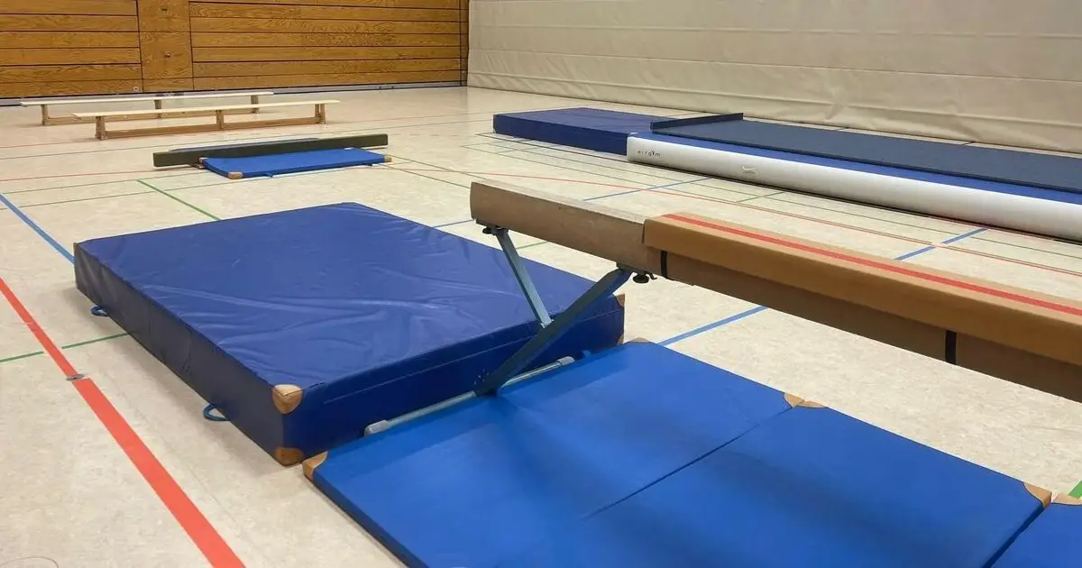 Turnhalle mit mehreren blauen Turnmatten und einem Schwebebalken auf dem Hallenboden