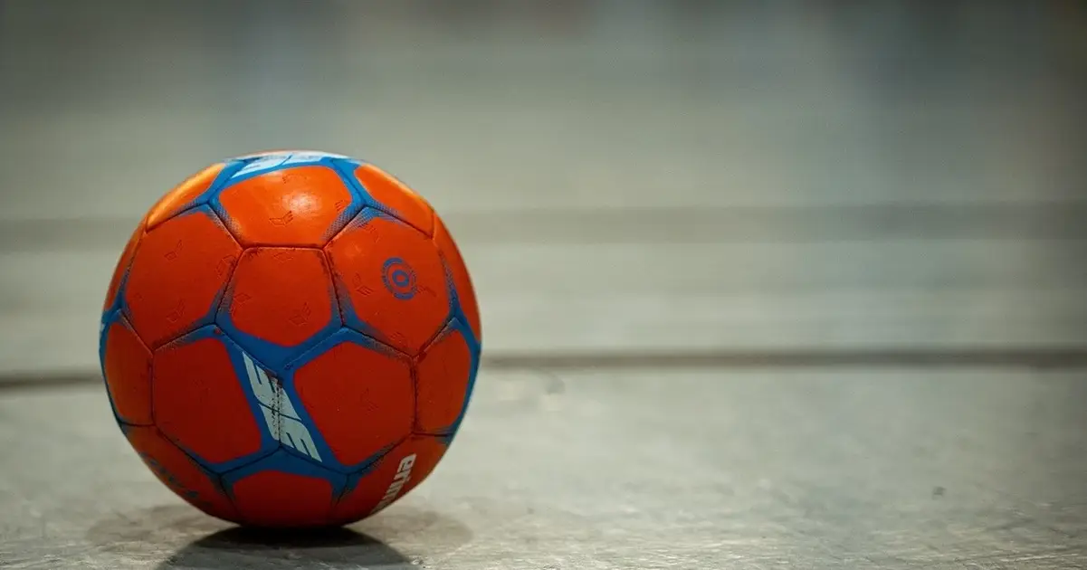 Ein Handball mit blau-orange Design liegt auf einem Spielfeld