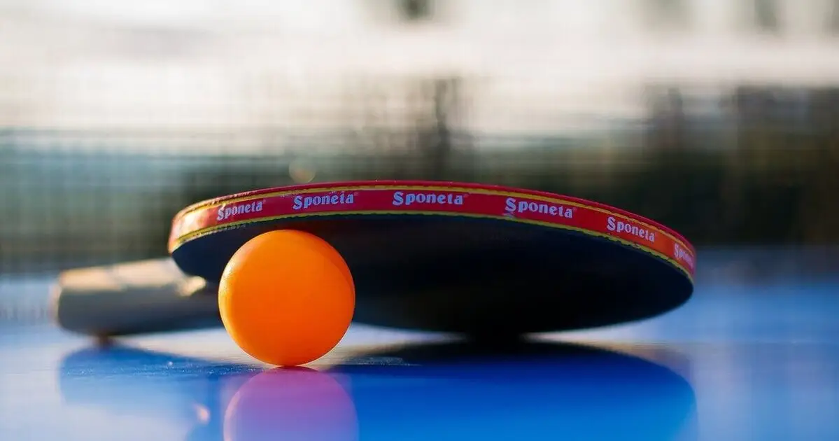 Ein Tischtennisschläger und ein orangener Tischtennisball liegen auf einer blauen Tischtennisplatte